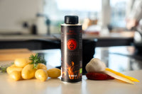 Eine Dose Turk Bio Bratöl der Albert Turk GmbH & Co. KG steht auf einer Küchentheke mit gelben Kartoffeln, Knoblauch, Rosmarin, rotem Chili und gelber Paprika. Im Hintergrund ist eine verschwommene Küche zu sehen.