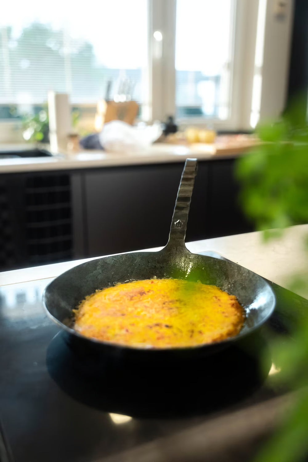 Die Geschmiedete Bratpfanne von Albert Turk GmbH & Co. KG steht mit einem Omelett auf dem Herd einer modernen Küche, während Sonnenlicht durch das Fenster scheint.