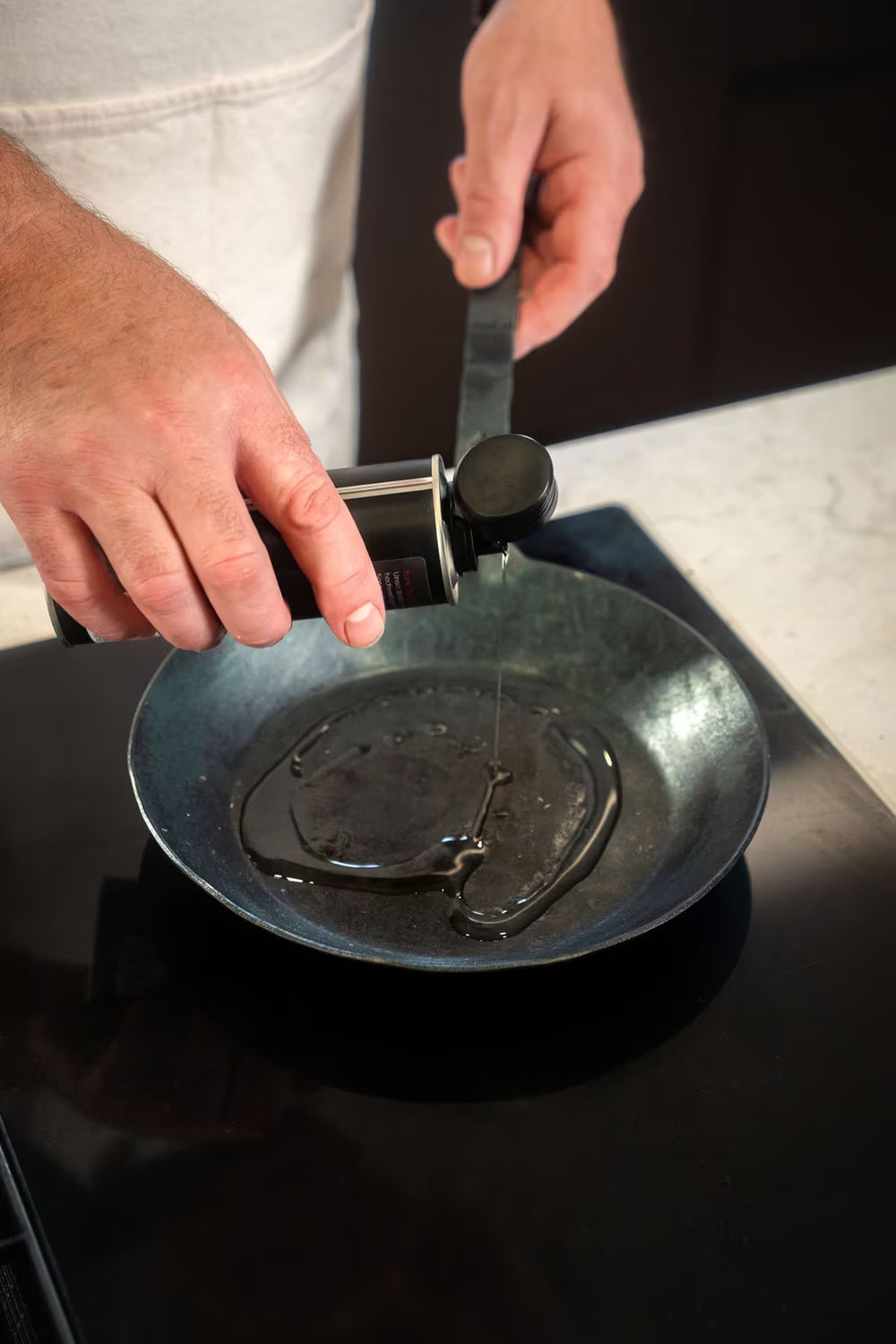 Jemand gießt Turk Bio Bratöl der Albert Turk GmbH & Co. KG in eine schwarze Bratpfanne auf dem Herd und macht sich bereit zum Kochen.
