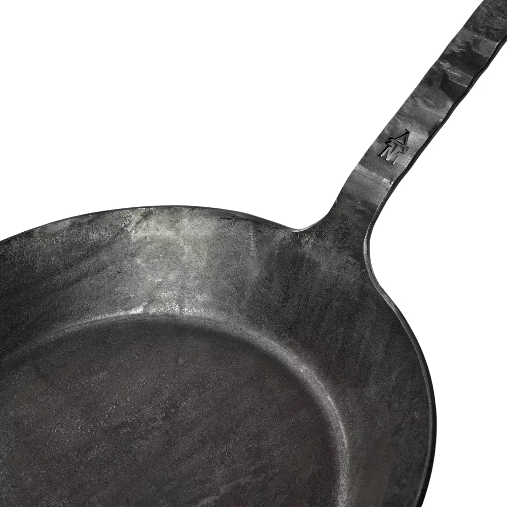 Nahaufnahme einer schwarzen Geschmiedeten Bratpfanne der Albert Turk GmbH & Co. KG, mit strukturiertem Griff und Haussymbol in der Nähe des Gelenks - ein elegantes Schaustück der Schmiedekunst, handgefertigt in Deutschland.